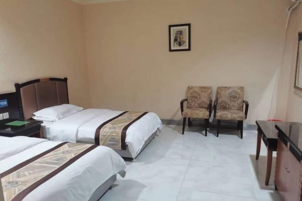 Une chambre d’hôtel avec deux lits, un bureau, une chaise et un tableau encadré au mur.