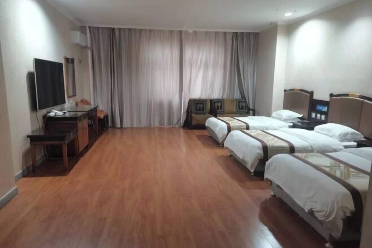 Une chambre d’hôtel avec un plancher en bois, un bureau avec une chaise, une télévision et trois lits avec du linge de lit blanc.