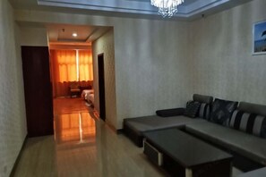 A modern hotel room with a sofa, a bench, and a hallway leading to a bedroom.