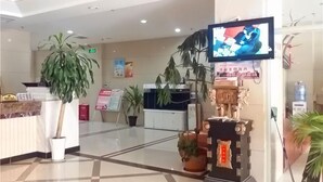 A reception area with a reception desk, potted plants, a television, and a water dispenser. - Changshou Business Hotel (Luntai)