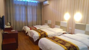 Habitación de hotel con tres camas, piso de madera, un escritorio con teléfono y un cesto de basura.