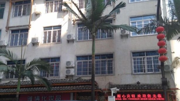 Un edificio de varios pisos con unidades de aire acondicionado, palmeras y diferentes comercios con letreros.