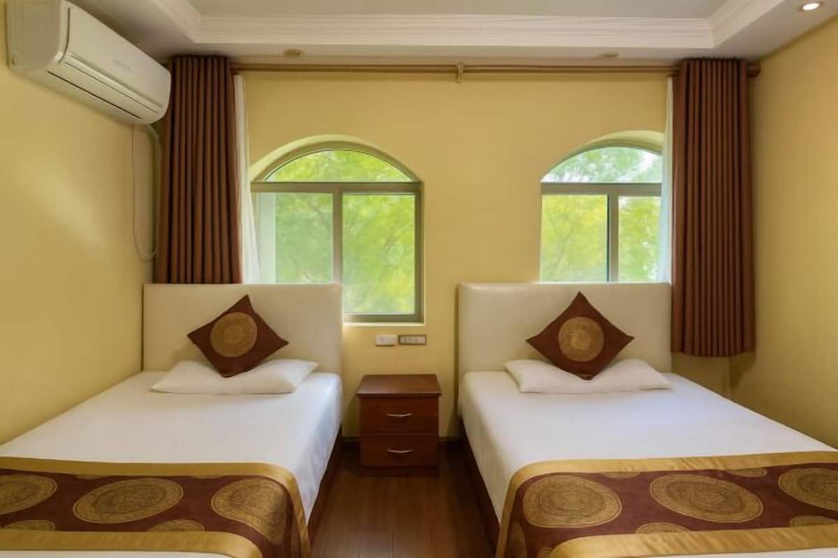 Ein Hotelzimmer mit zwei Einzelbetten, einem Nachttisch, einer Klimaanlage und einem Fenster mit Vorhängen.