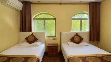A hotel room with two single beds, a nightstand, an air conditioning unit, and a window with curtains.