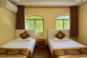 Une chambre d’hôtel avec deux lits simples, une table de chevet, un appareil de climatisation et une fenêtre avec des rideaux.