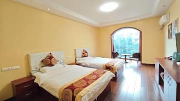 A hotel room with two beds, a small table, a chair, and a window.