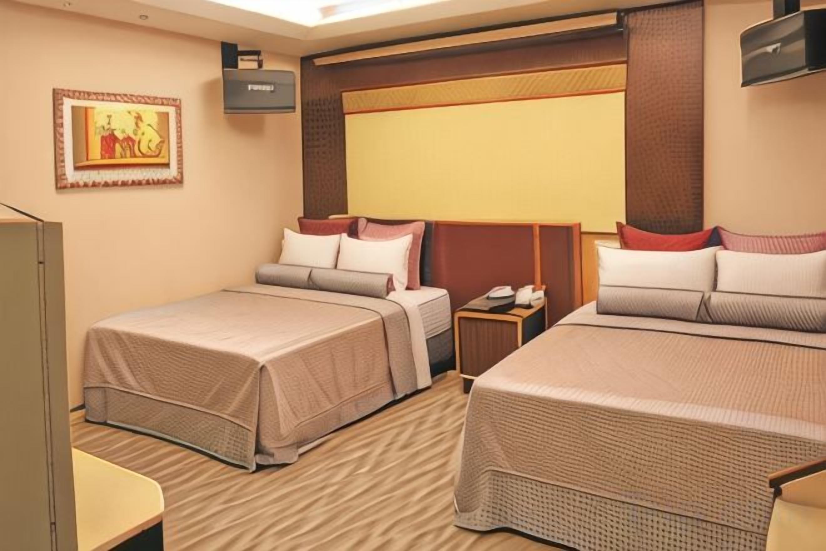 A hotel room with two beds, a desk, a chair, a TV, and a wall-mounted artwork.