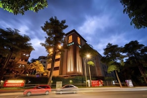 A modern building with illuminated signage, surrounded by trees and a street with passing cars. - In-Stone Motel (Taipei)
