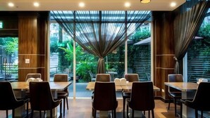 Restaurante moderno com área de jantar central, mesas e cadeiras, rodeado por grandes janelas com vista para áreas verdes.