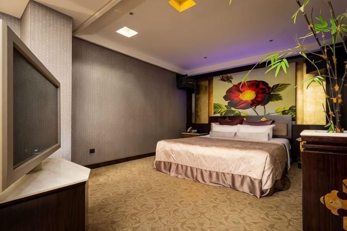 Een hotelkamer met een groot bed, een flatscreen televisie, een bureau en een groot raam met een bloemschilderij.