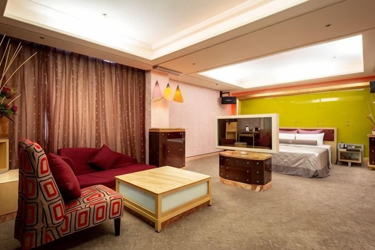 Een hotelkamer met een bank, een houten salontafel, een televisie, een bed en een klein bureau.