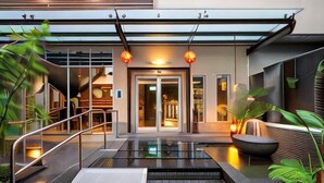 Entrada de hotel moderna com porta de vidro, área de estar externa e uma pequena piscina.