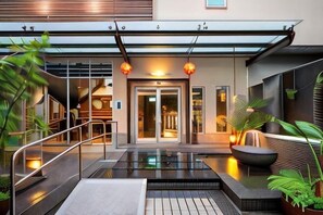 A modern hotel entrance with a glass door, outdoor seating, and a small pool area. - In-Stone Motel (Taipei)
