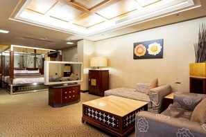 Une chambre d’hôtel avec un lit, un canapé, une table basse, une télévision, un miroir et un tableau au mur.