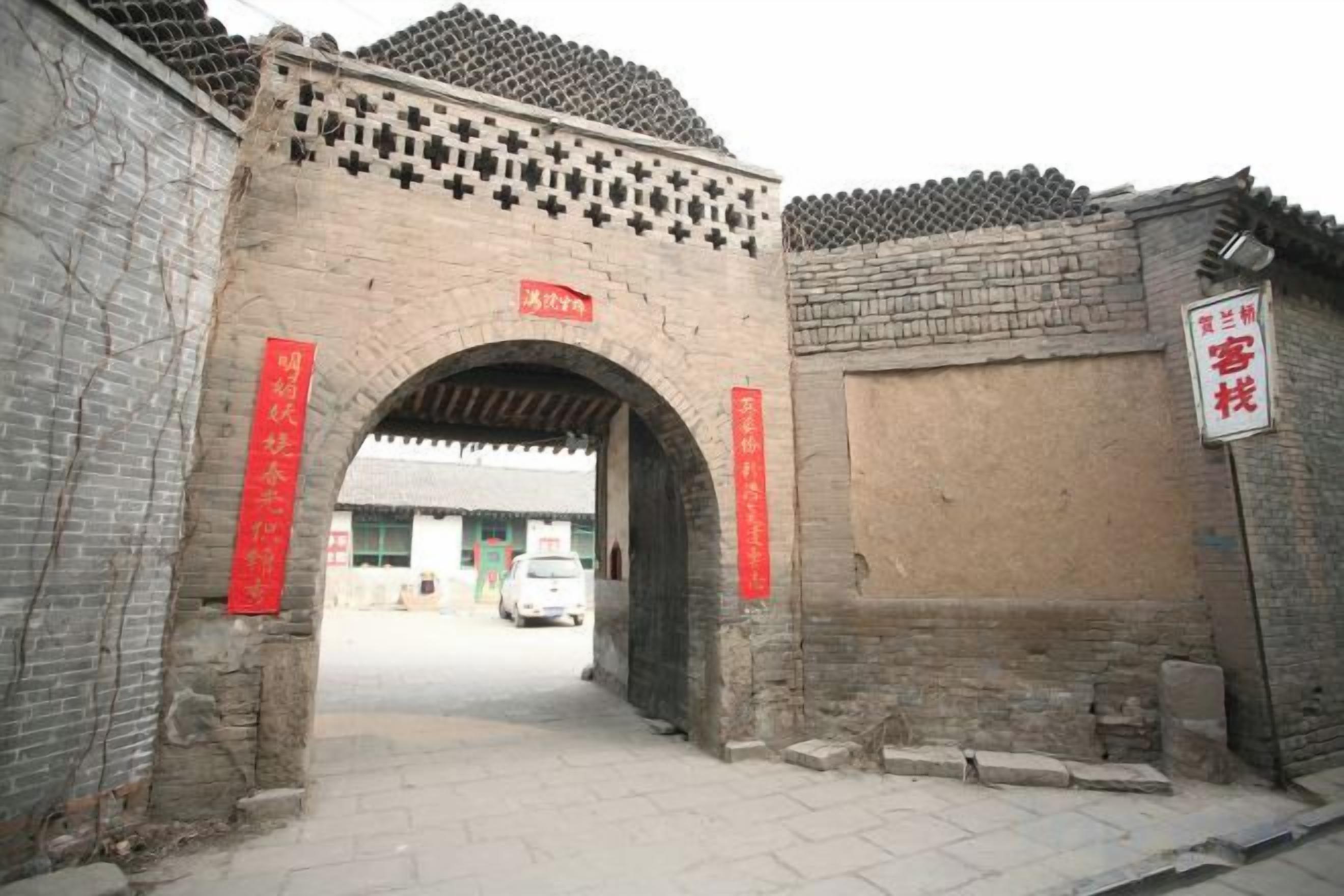 An arched entrance with a tiled roof, a brick wall, and a red sign.