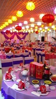Un salón de banquetes con mesas redondas, manteles morados y blancos, y faroles rojos.