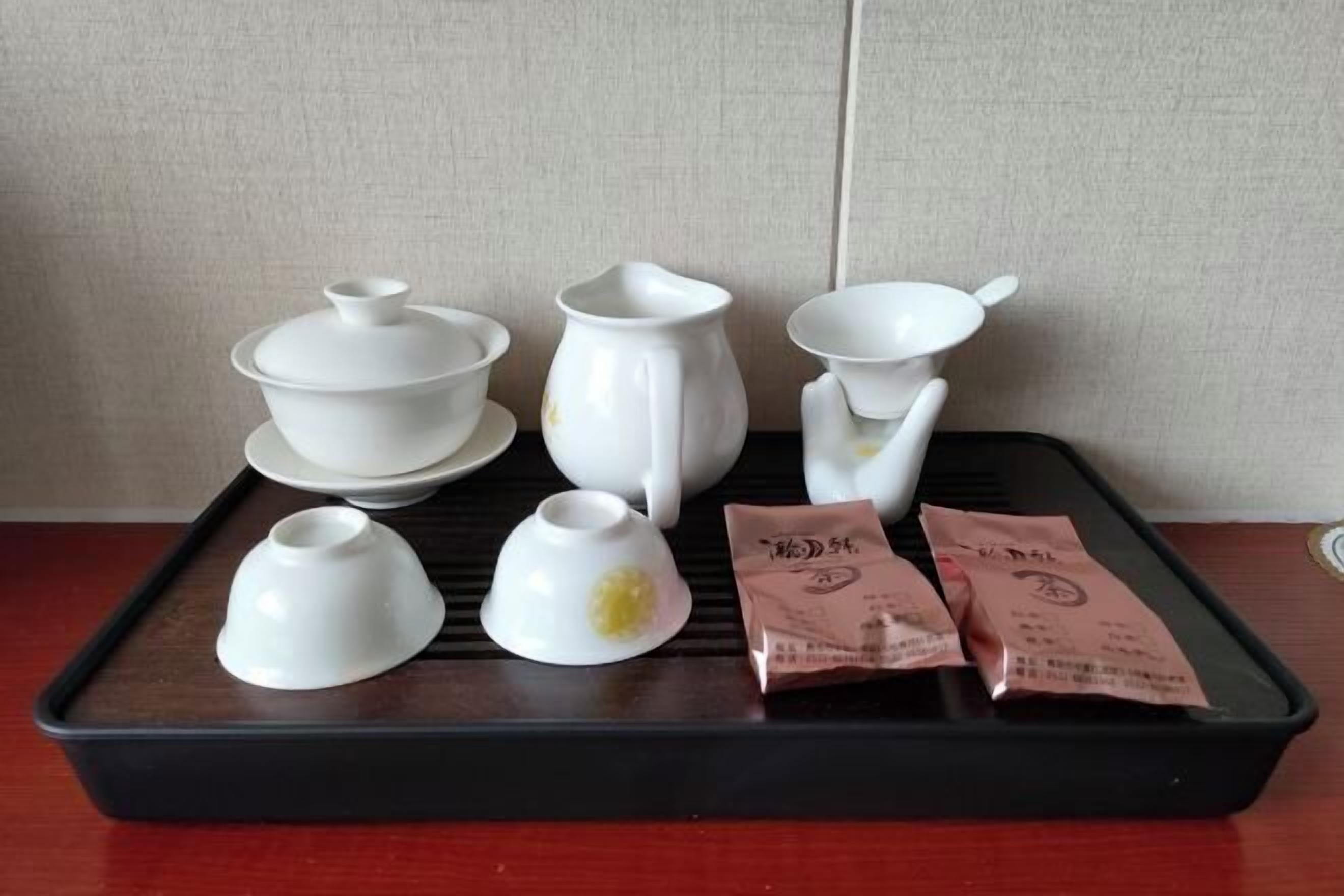 A tray with white ceramic tea set, including a teapot, cups, and saucers, alongside two tea bags.