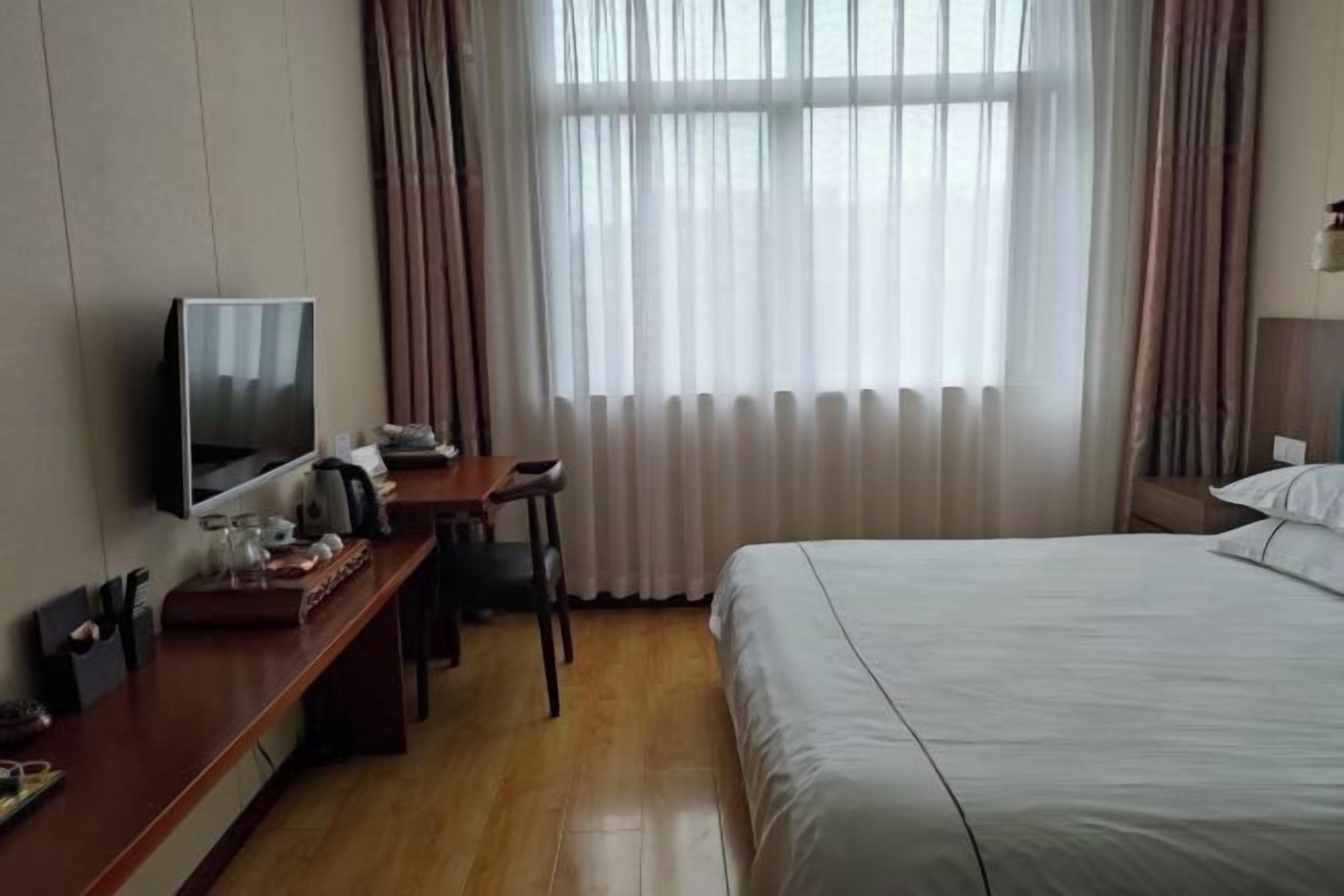 A hotel room with a bed, a desk with a television, a chair, and a window with curtains.