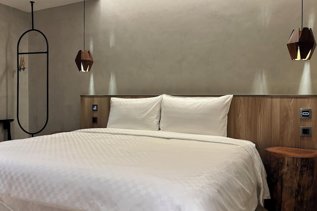 Ein modernes Hotelzimmer mit einem großen Bett, einem Holz-Kopfteil und zwei Nachttischen.
