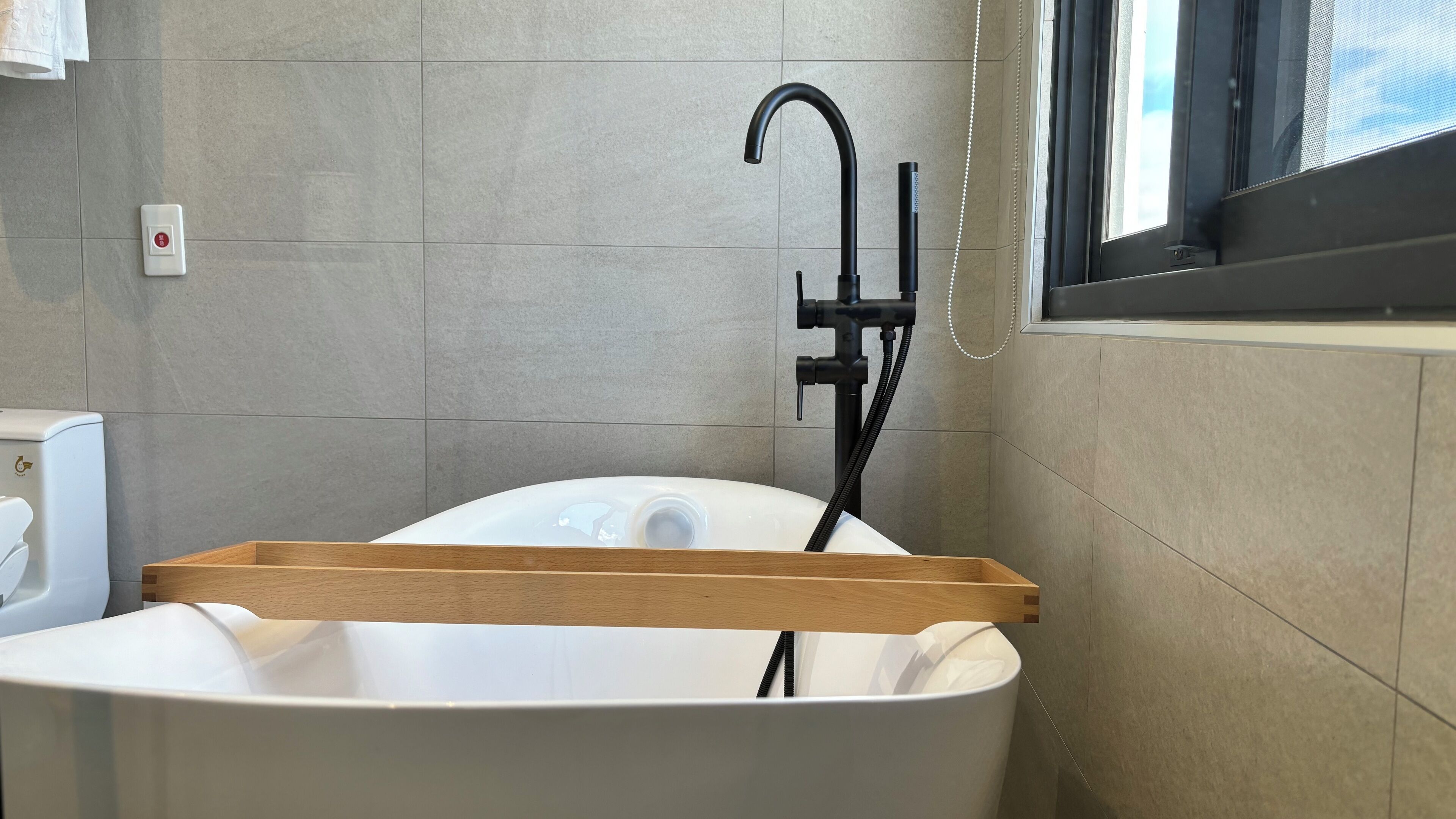 A modern bathroom with a freestanding bathtub, a handheld showerhead, and a towel rack.