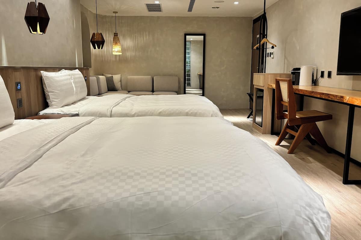 Ein Hotelzimmer mit zwei Betten, einem Schreibtisch mit Stuhl, einem Fernseher und einem Spiegel.