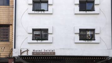 En hotellfasad med flera fönster, en skylt som visar att det är ”Hotel Initial”, och en traditionell arkitektonisk stil med ett utskjutande tak av trä.