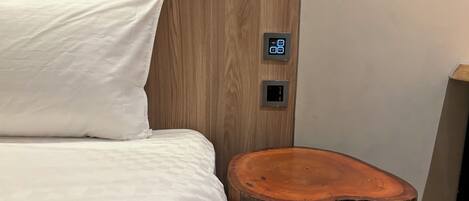 A neatly made bed with white linens, a wooden headboard, and two wall-mounted control panels.