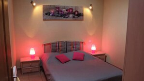 A bedroom with a bed, two bedside tables, and a wall-mounted shelf with candles. - Ferme en Cévennes (Aulas)