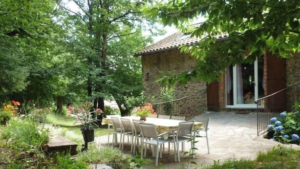 A stone building with a patio area featuring a table and chairs. - Ferme en Cévennes (Aulas)
