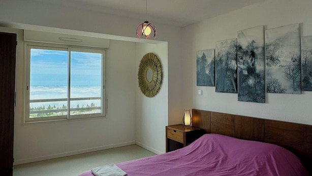 A bedroom with a large bed, a window with a view, a wall-mounted light fixture, and a painting. - Appartement 6 Places à 150m des Pistes (Arette)