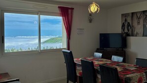 A dining area with a table set for four, a television, and a view of the sea through large windows. - Appartement 6 Places à 150m des Pistes (Arette)
