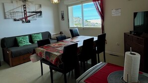 A living room with a dining table, sofa, and a TV. There is a window with a view of the outdoors. - Appartement 6 Places à 150m des Pistes (Arette)
