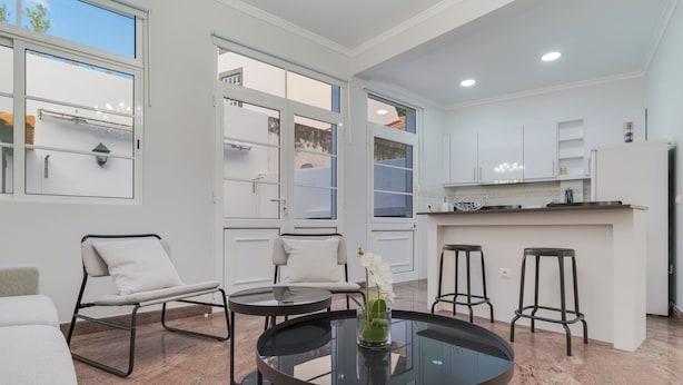 A modern kitchen with white cabinets, a black countertop, and a small bar area. There are two white chairs and a round glass table with a vase of flowers. - Funchal City Nest I (Funchal)