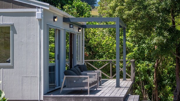 Une terrasse en bois dotée d’un espace salon couvert et d’une porte vitrée donnant sur une pièce.