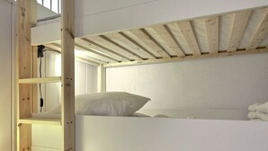 Ein Stockbett mit Holzleiter, weißer Bettwäsche und einer weißen Wand.