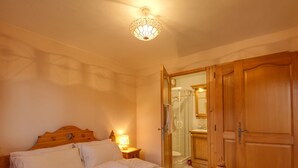 A bedroom with a wooden bed, a nightstand with a lamp, a wooden wardrobe, and a glass shower enclosure. - Beautiful 3-bed apartment, ski-in with wifi (Morillon 1100)