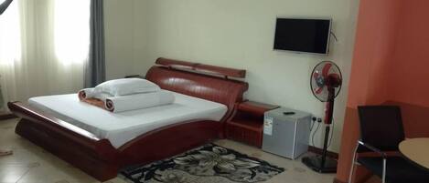 Una habitación de hotel con una cama, televisión, ventilador y escritorio.