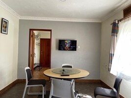 Una habitación con una mesa redonda, sillas, un televisor en la pared y una puerta que da a otra estancia.