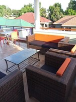 Mobiliario de mimbre exterior con cojines, una mesa de vidrio y vistas a edificios en la distancia.