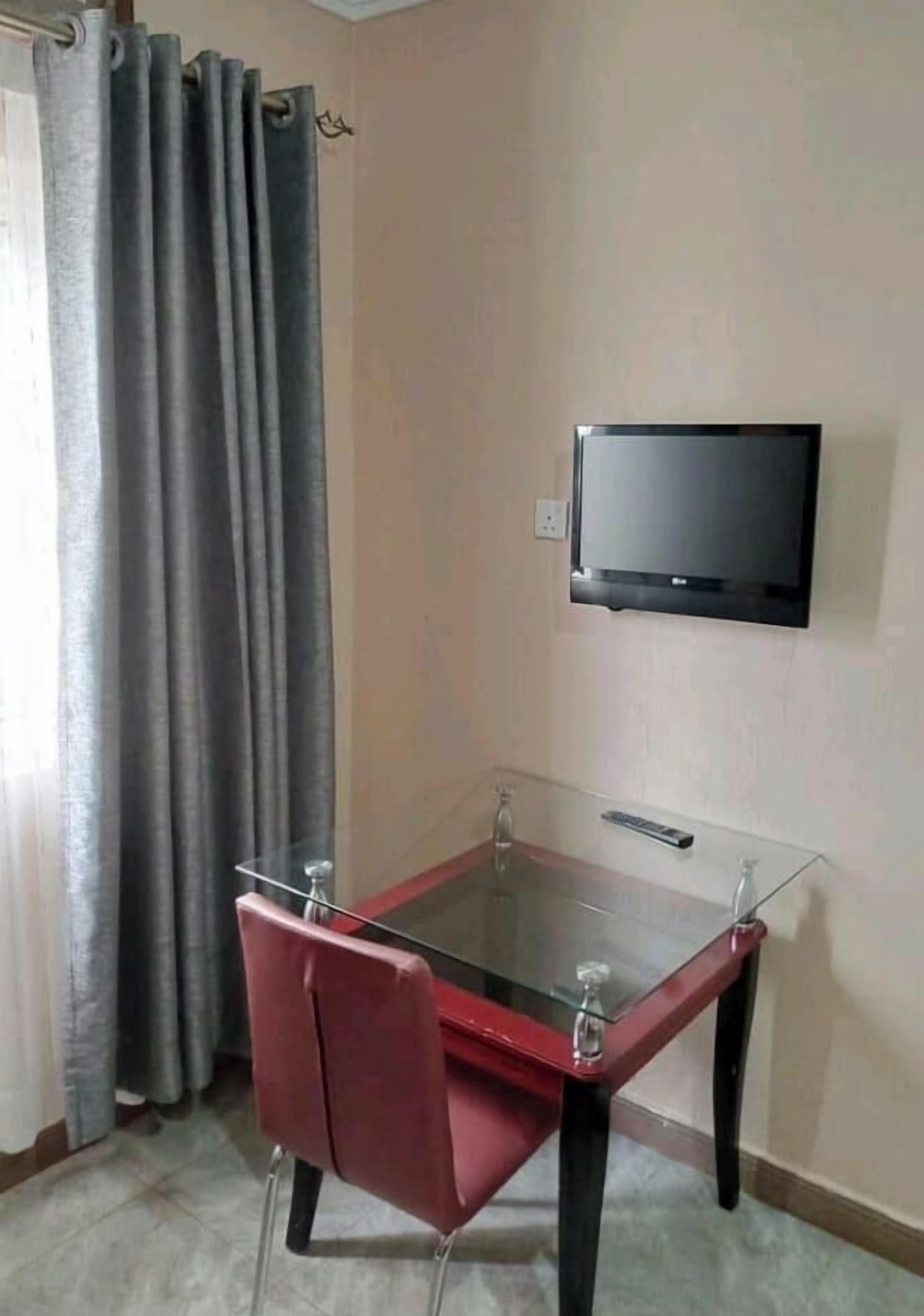 A room with a glass table, red chairs, a television mounted on the wall, and a curtain.