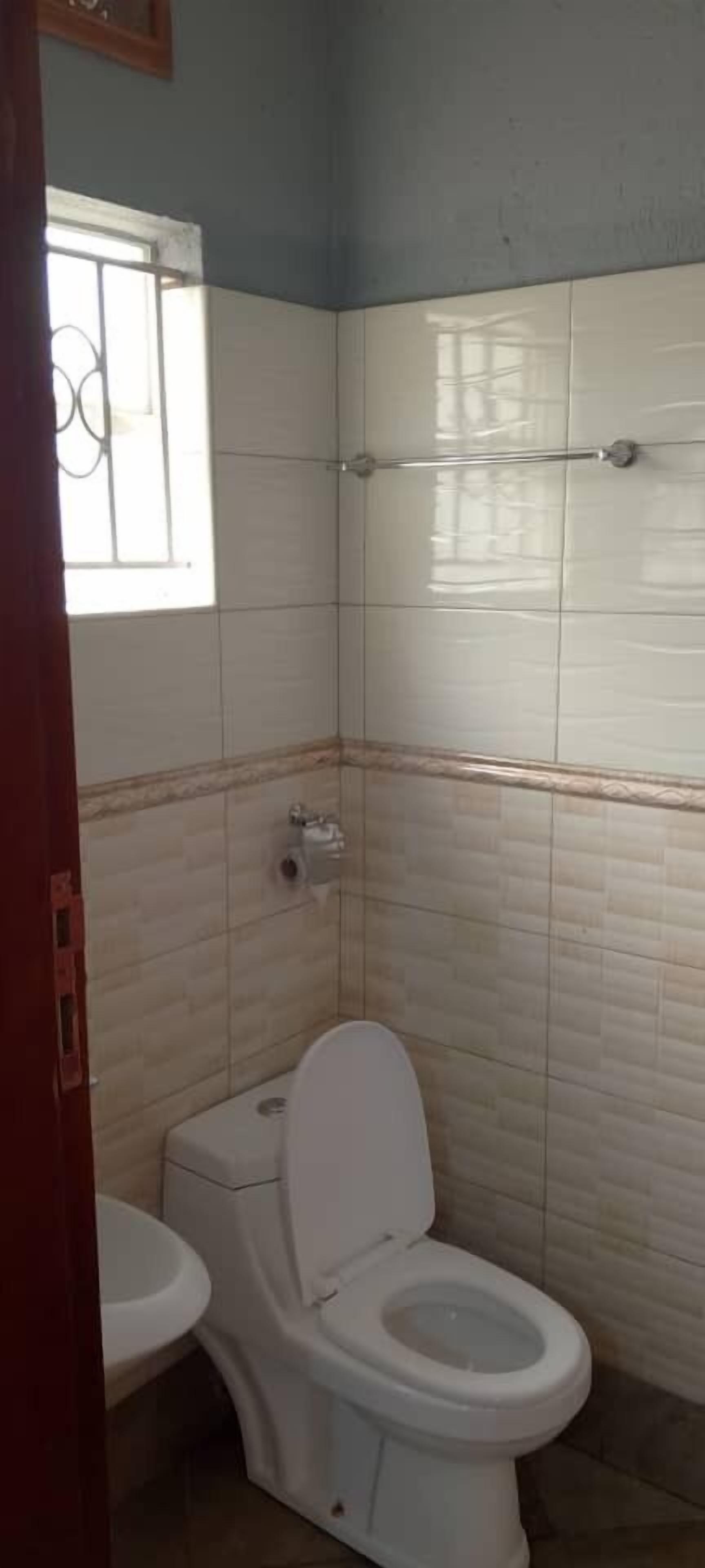 Et badeværelse med toilet, håndvask og et vindue med tremmer.