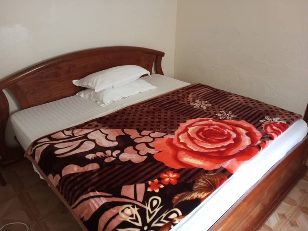 A bed with a floral-patterned bedspread, a wooden headboard, and a white pillow.