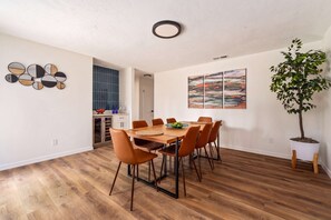 A dining area with a wooden table and chairs, a potted plant, and artwork on the walls. - The Monterey | Private Pool • Grill • 4 King Beds (Gainesville)