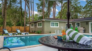 Quintal com piscina, cadeiras de lounge e mesa de pátio coberta.