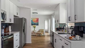 Uma cozinha moderna com armários brancos, eletrodomésticos de aço inoxidável e um espaço de refeições de madeira com uma cadeira e mesa.