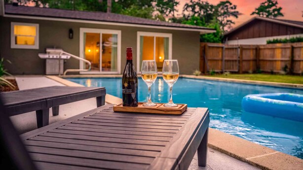 Cenário à beira da piscina com uma mesa, uma garrafa de vinho e dois copos.