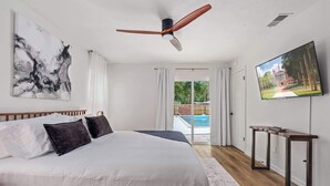 Quarto com uma cama grande, um ventilador de teto, uma TV e vista para uma piscina.