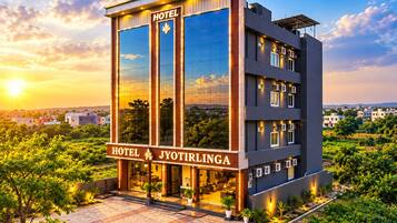 A modern hotel building with a glass facade, a sign reading 'HOTEL JYOTIRLINGA,' and a paved entrance area with potted plants.