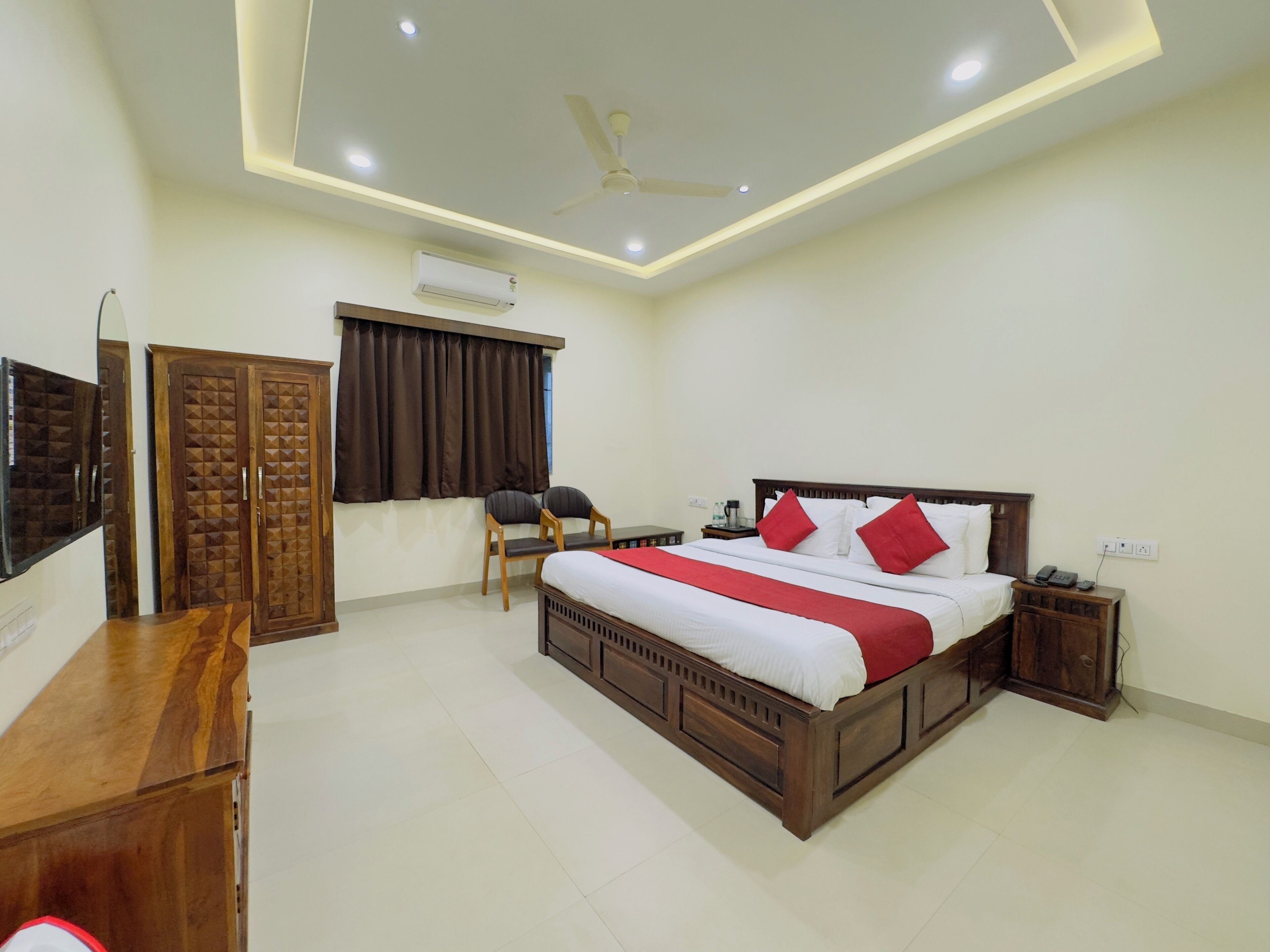 A hotel room with a wooden bed, a desk, a chair, a wardrobe, and a ceiling fan.