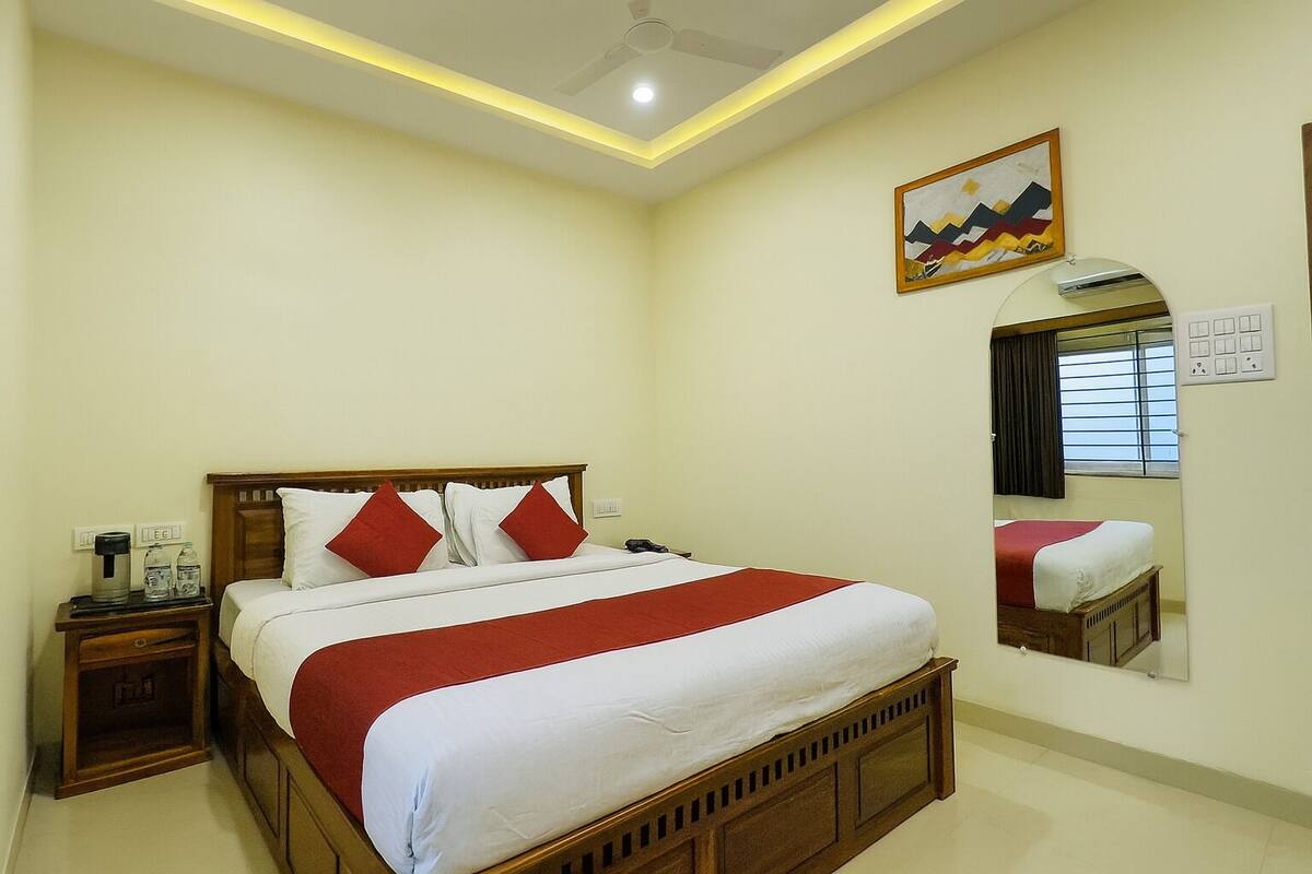 Habitación de hotel con una cama grande, una mesita de noche con lámpara, un espejo y un cuadro en la pared.
